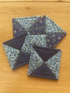 four pieces of blue and green fabric on a wooden table with one piece folded in the shape of an origami