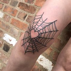 a person with a spider web tattoo on their arm and leg, next to a brick wall