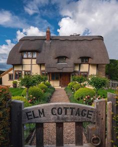 a thatched roof house with a wooden gate and sign in the foreground saying elm cottage