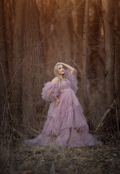 a woman in a pink dress standing in the woods with her hands on her head