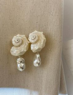 This is a pair of handcrafted white conch shell earrings with pearl pendants, crafted from natural conch shells and featuring s925 silver studs. The design is unique and exquisite, making them a perfect and special gift. Material - Conch, Pearl, s925 Silver - Free shipping. - Handcrafted, packaged in an exquisitely designed gift box, perfect for gifting. - Order processing time: 3-7days. Conch Jewellery, White Pearl Shell With Pearl Pendant, Pearl White Shell With Pearl Charm, White Shell-shaped Pearl Earrings, Elegant Pearl Shell With Pearl Drop, White Shell Dangle Pearl Earrings, White Shell With Pearl Charm, White Dangle Shell Pearl Earrings, White Shell With Pearl Pendant