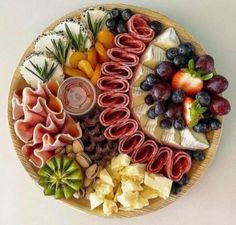 a platter filled with fruit, crackers and cheeses on top of a wooden plate