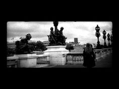 a black and white photo of people walking on a bridge with statues in the background