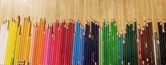 many different colored pencils lined up in a row next to each other on a wooden surface