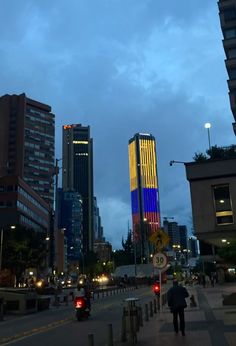 a city street with tall buildings and people walking on the side walk at night time