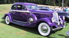 an old purple car parked on top of a grass covered field next to other cars