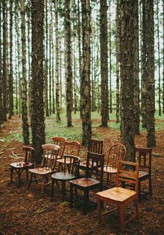 several wooden chairs and tables in the middle of a forest with tall trees behind them