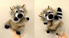 two stuffed raccoons are being held up by someone's hand in front of a white wall