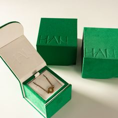 two green boxes with necklaces in them sitting next to each other on a white surface