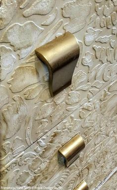 two brass handles on an ornate white cabinet with intricate embosishments and floral designs