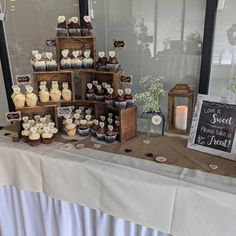 a table topped with lots of cupcakes covered in frosting next to a window