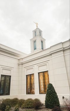 a white building with a steeple and windows on the top floor is surrounded by shrubbery