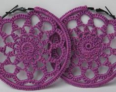 two purple crocheted earrings are shown on a white surface, one is circular and the other is round