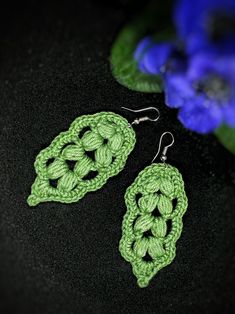 green crochet earrings on black surface with blue flowers in the backgroud