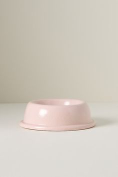 a pink dog bowl sitting on top of a white table next to a black cat