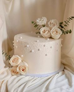 a white wedding cake with roses on top and pearls around the edges is sitting on a table