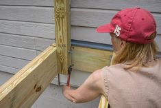 a woman in a red hat is working on the side of a house with wood