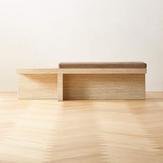 a bench sitting on top of a hard wood floor next to a wall with a white background