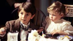 two young children sitting at a table with plates of food and drinks in front of them