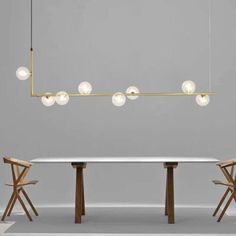 a table with chairs and lights hanging from it's ceiling in front of a gray wall