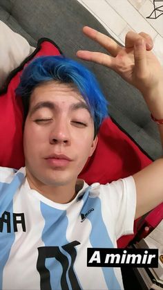 a young man with blue hair is making the peace sign while laying down in bed