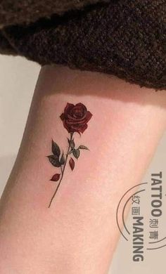 a small rose tattoo on the left side of the arm, with green leaves and red flowers