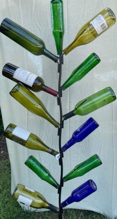 a tree made out of wine bottles sitting on top of a grass covered field next to a white tarp