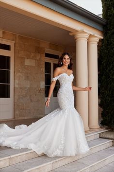 a woman in a white wedding dress standing on some steps and posing for the camera