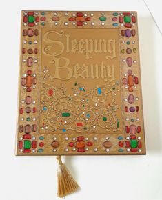 a wooden sign with beads and tassels on it that says sleepy beauty in gold lettering