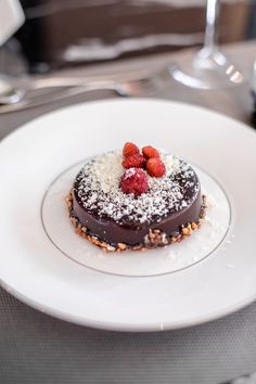 a chocolate dessert with powdered sugar and raspberries is on a white plate