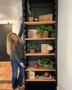 a woman standing next to a book shelf filled with plants