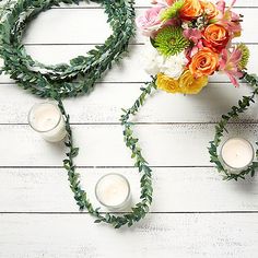 flowers and candles are arranged on a white wooden surface with greenery around them,