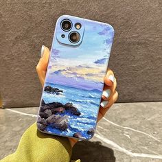 a person holding up a phone case with an image of the ocean and rocks on it