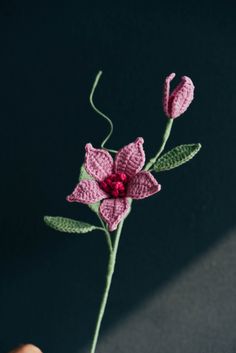 a crocheted pink flower with green leaves is held by someone's hand