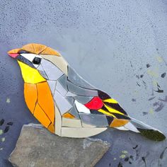 a bird made out of stained glass sitting on top of a piece of rock in the water