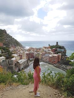 a woman standing on top of a hill looking at the water and buildings in the background