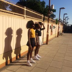 two young women standing next to each other near a wall with their shadows on it