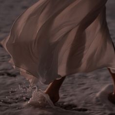 a woman is walking in the water with her dress flowing over her legs and feet