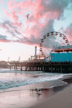 a ferris wheel sitting on top of a pier next to the ocean under a pink sky