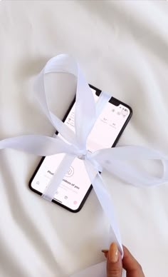 a person holding an iphone with a white ribbon tied around it and another cell phone in the background