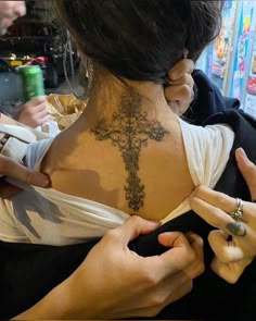 a woman with a cross tattoo on her back is looking at her cell phone while she's holding the other hand