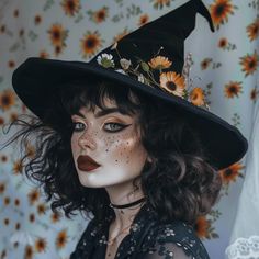 Modern sassy Gen Z witch with beautiful green eyes, makeup and freckles. Her pointed witch hat is decorated with daisies and marigold flowers, matching the curtain in the background. Brunette in a black blouse with a floral pattern. Witchy Looks Makeup, Fall Witch Makeup, Orange And Black Witch Makeup, Witch Inspo Halloween, Beautiful Witch Costumes, Curly Witch Hair, Natural Witch Costume, Green Witch Costume For Women, Aesthetic Witch Makeup