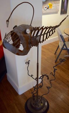 a metal fish skeleton sitting on top of a wooden floor next to a white wall