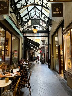 people are sitting at tables in the middle of an open air shopping mall with glass ceilings