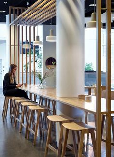 a woman sitting at a long table in a room with lots of wooden stools