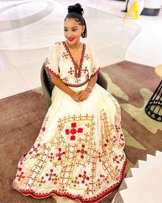 a woman sitting in a chair wearing a white dress with red and gold designs on it