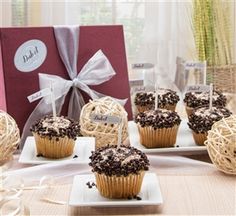 chocolate cupcakes are sitting on small plates next to a red box with a bow