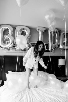 a woman standing on top of a bed surrounded by balloons