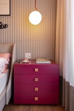 a pink chest of drawers next to a bed