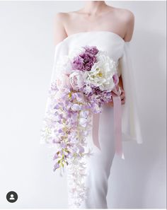 a woman in white dress holding a purple and white bouquet with flowers on it's back